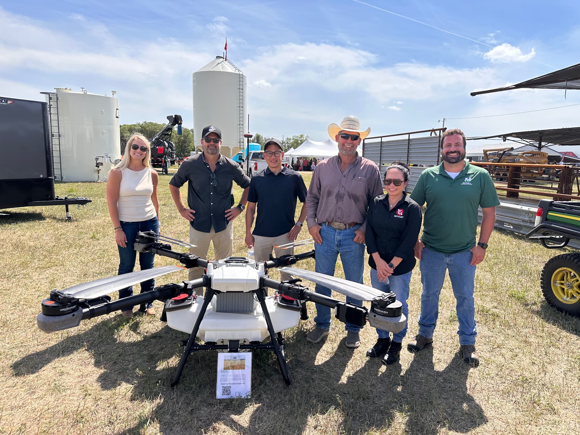 The DroneDash Technologies and GEODNET team standing behind a large GEODASH agricultural spraying drone at a field demonstration in the United States